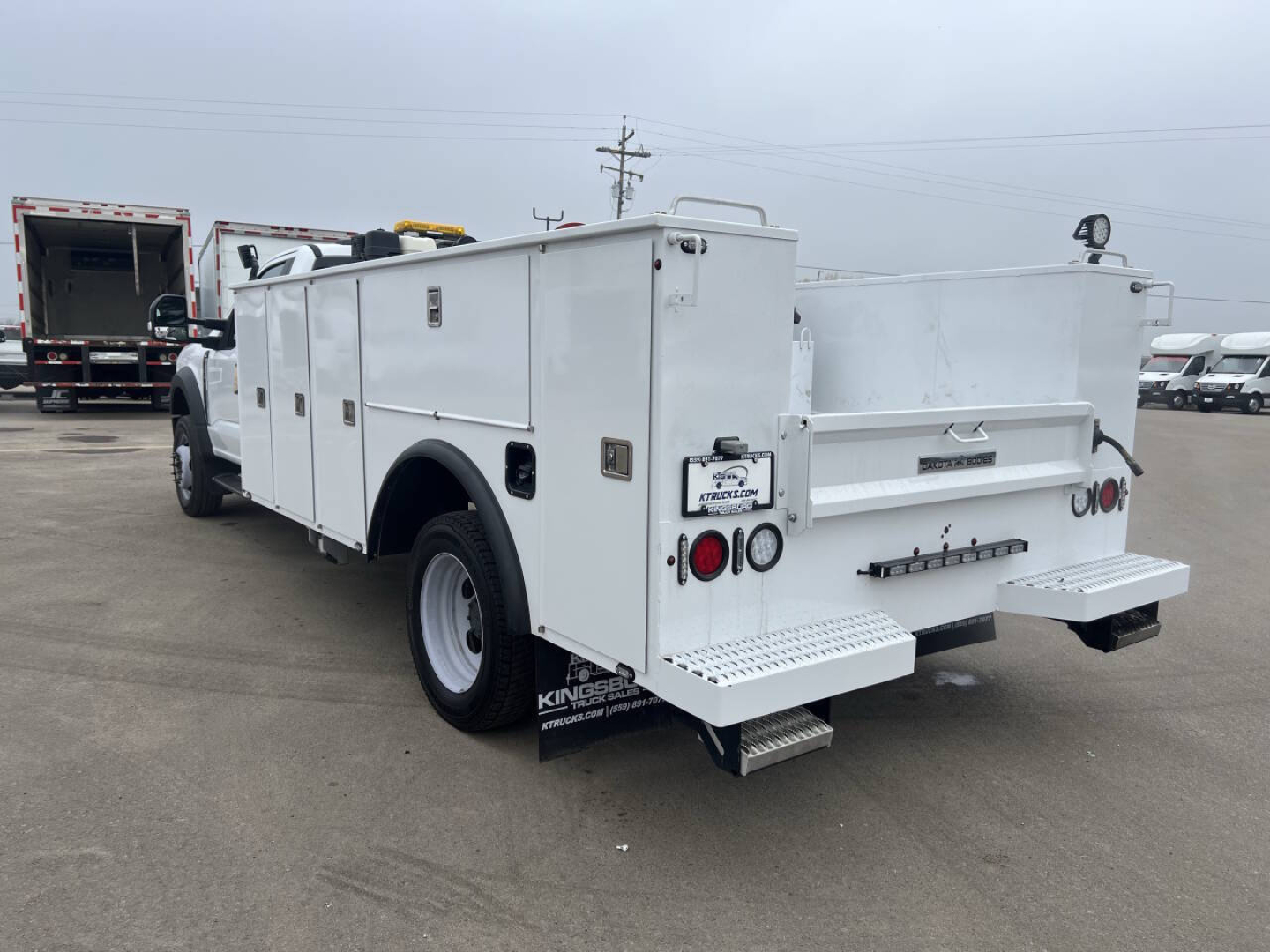 Service/utility truck rear and side view showing compartments, utility body, rear steps, and bumper light cluster on a white Ford F-550.