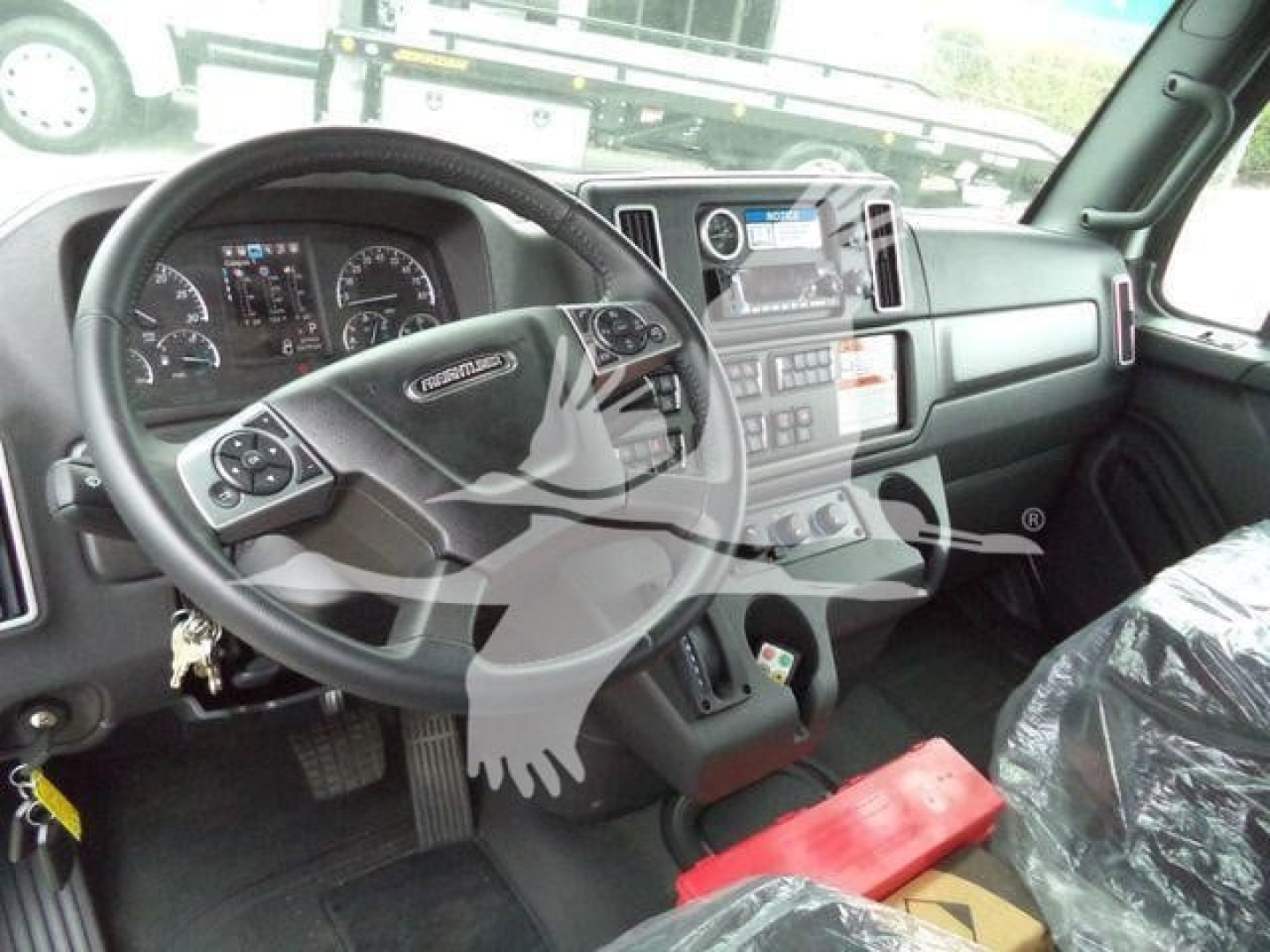 Freightliner M2 106 truck cab interior showing steering wheel, dashboard, control panel, and center console; plastic seat cover on passenger seat.