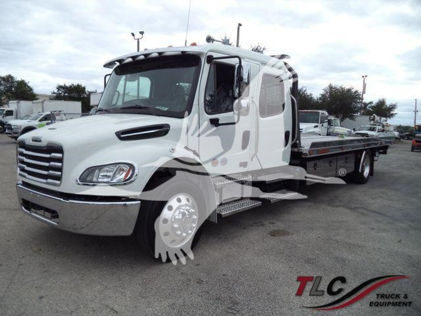 Flatbed tow truck on lot with white Freightliner M2 106 cab, side steps, and rolling bed trailer.