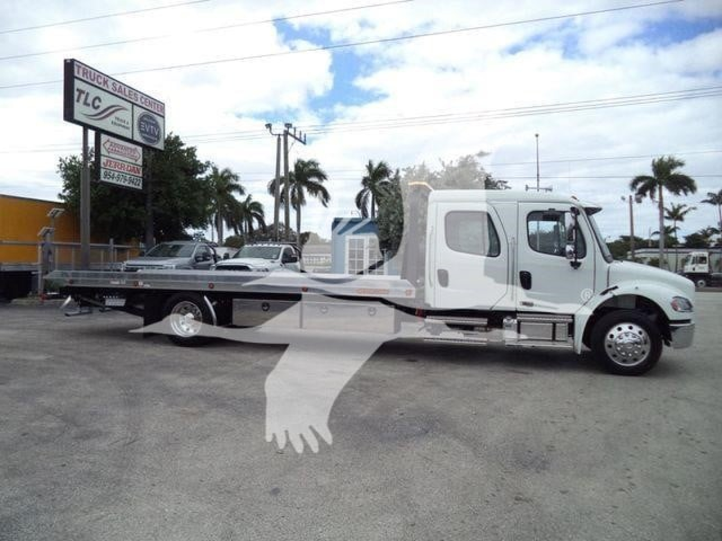 Freightliner M2 106 rollback tow truck in a dealership lot with extended flatbed and white cab.