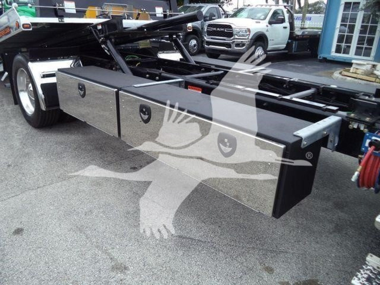 Front-left view of a Freightliner M2 106 rollback chassis showing large aluminum toolbox drawers along side, with hydraulic lines and truck bed frame in background.