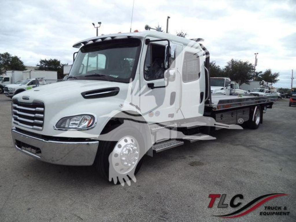 Flatbed tow truck on lot with white Freightliner M2 106 cab, side steps, and rolling bed trailer.