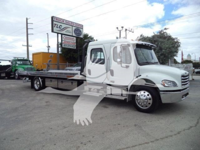Freightliner M2 106 rollback truck side view showing long flatbed and dual rear wheels with white cab.