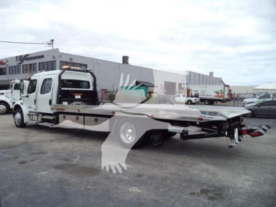 Truck bed with a white Freightliner M2 106 rollback tow truck chassis and flatbed, rear view shows equipment and hitch points.