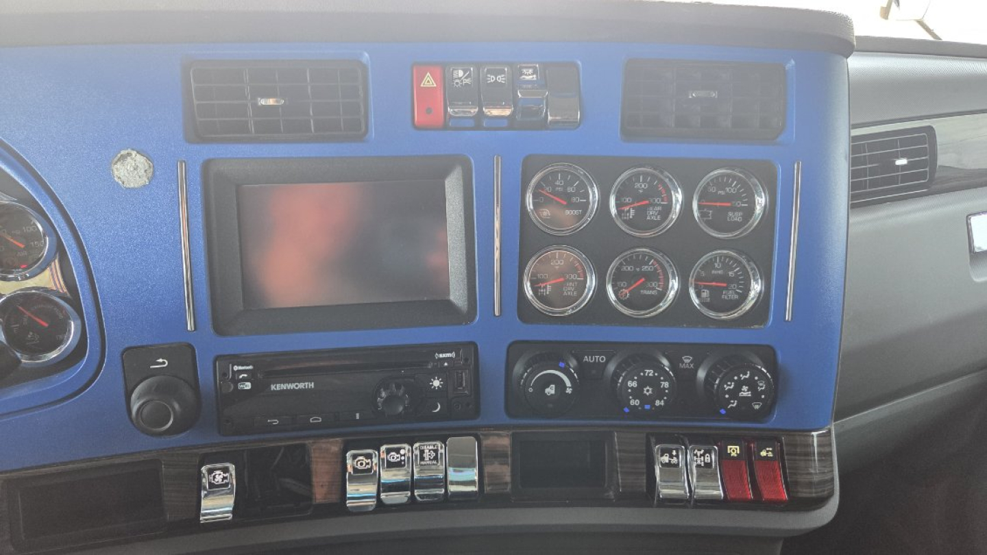 Kenworth T680 dashboard view showing multiple gauges, touchscreen display, climate controls, and switch panel.