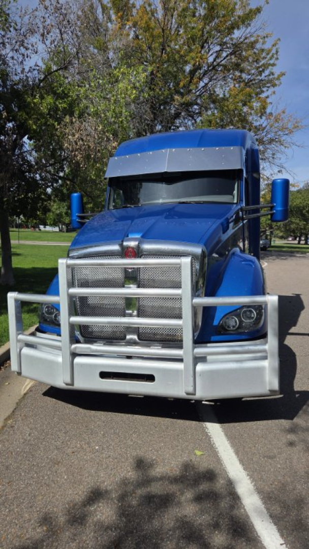 Kenworth T680 truck front view in blue with protective grille and bumper guard. The large chrome grille and headlights are visible.