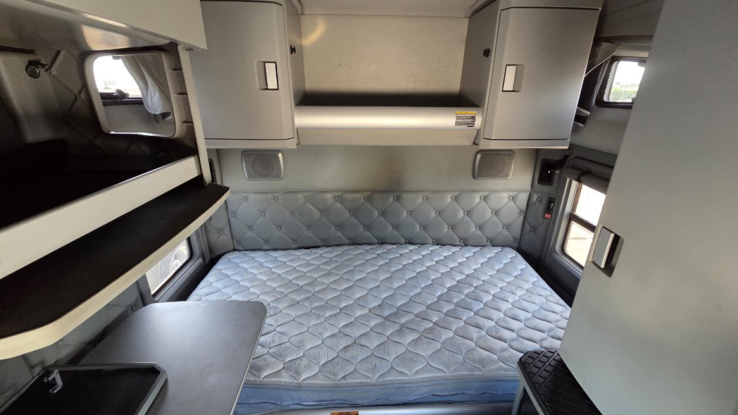 Kenworth T680 sleeper cab interior with quilted mattress and overhead storage compartments.