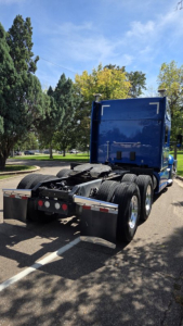 Kenworth T680 tractor in blue, rear view showing dual rear axles and fifth wheel, trailer hitches, and mud flaps.