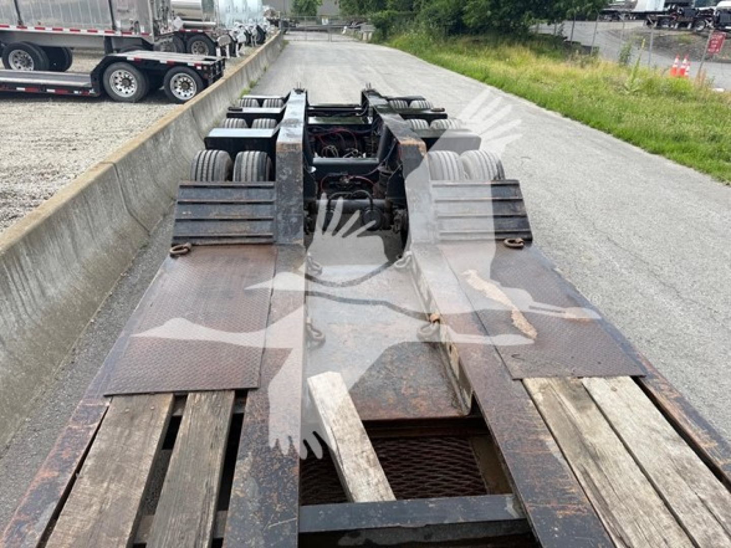 Lowboy trailer deck in view showing dual rear axles and wooden deck sections with metal framing and rusty surfaces.