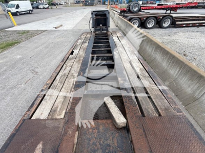 Lowboy trailer bed with steel beams and supports, rust tones, open center, and a wooden deck in the middle.
