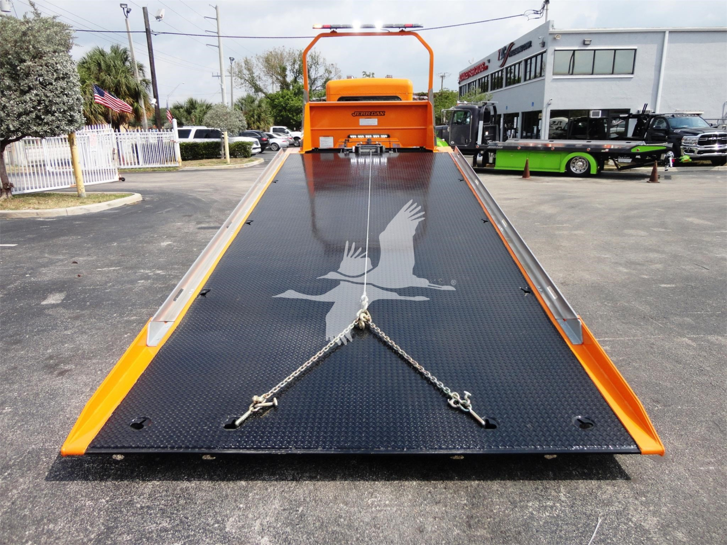 Front-facing view of a bright orange 2022 Peterbilt 337 rollback bed with a black diamond-plate steel ramp, eagle decal, and towing chains centered on the ramp.
