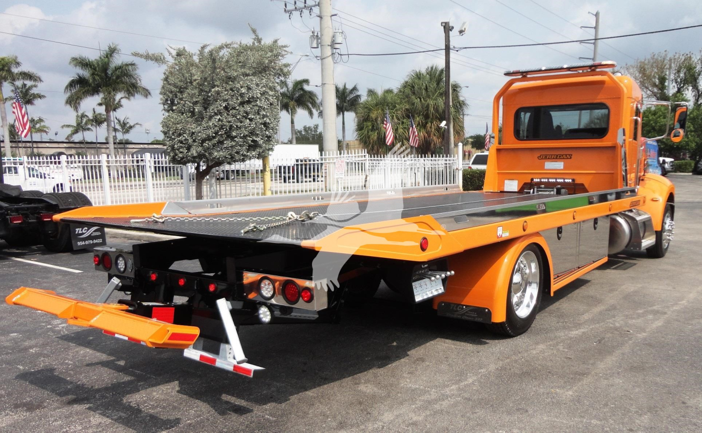 Tractor unit with bright orange rollback trailer showing platform and rear staging, Peterbilt 337 tag, cab visible on right.