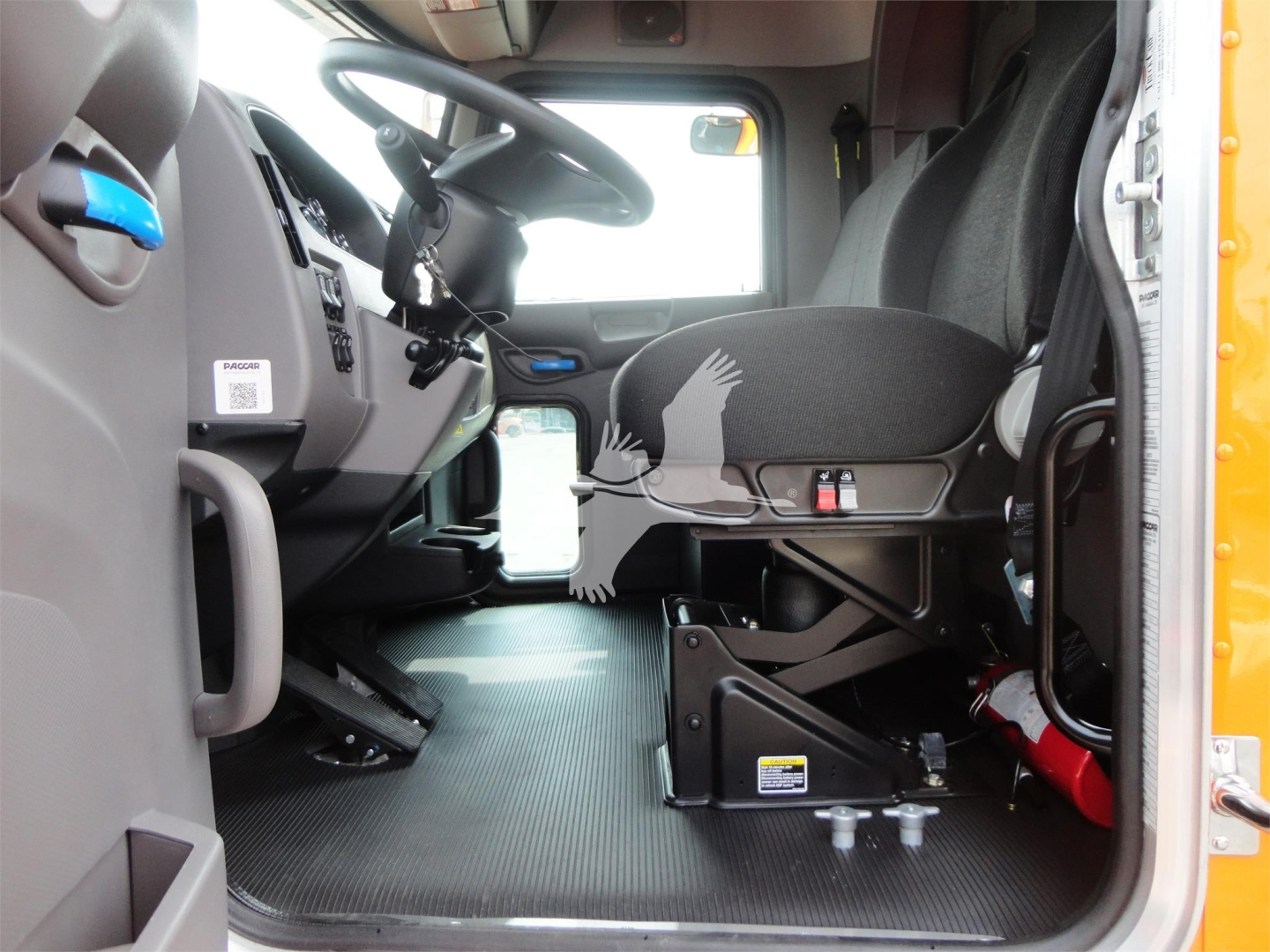 Truck cab interior showing driver's seat and dashboard of a 2022 Peterbilt 337. Visible text includes emission warning label on the driver side, and a QR code label near dashboard.