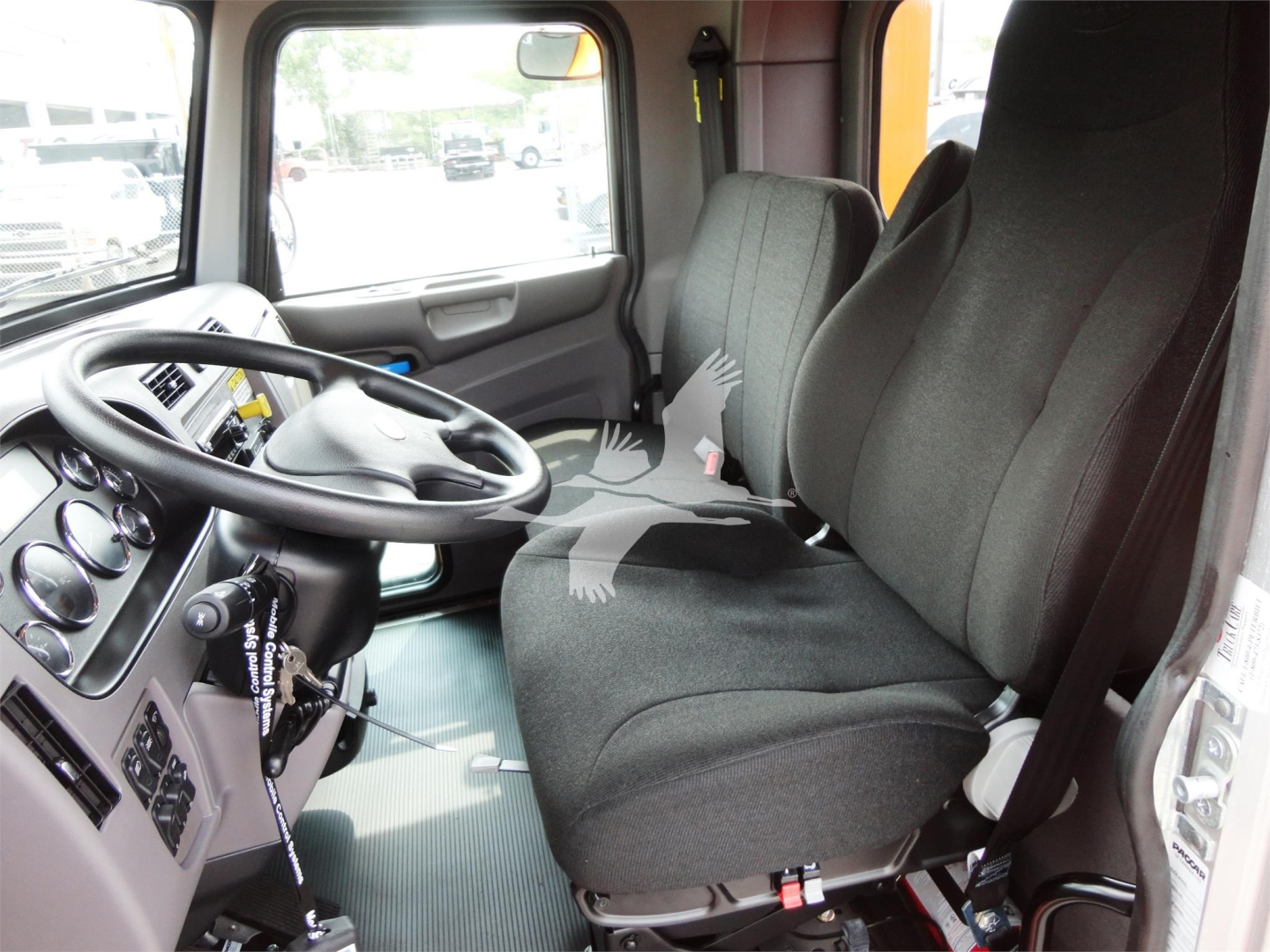 Truck cab interior showing steering wheel, driver's seat, and passenger seats in a 2022 Peterbilt 337 under showroom lighting.