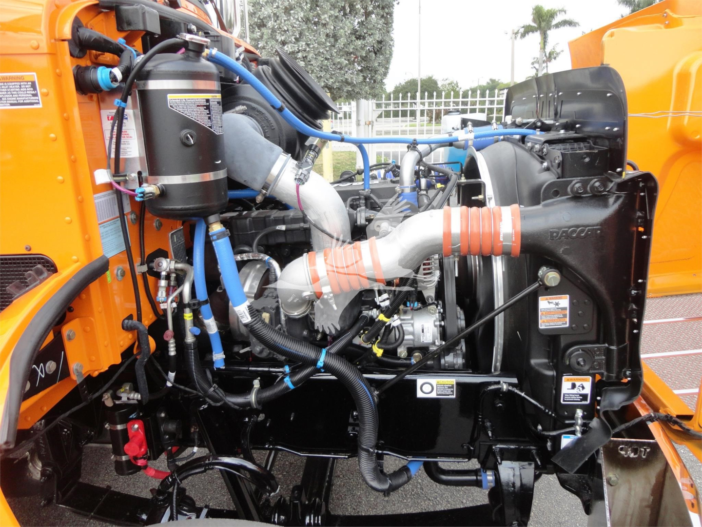Peterbilt 337 engine bay with visible hoses, clamps, turbo, intercooler, and wiring; factory orange body panels and black engine components.
