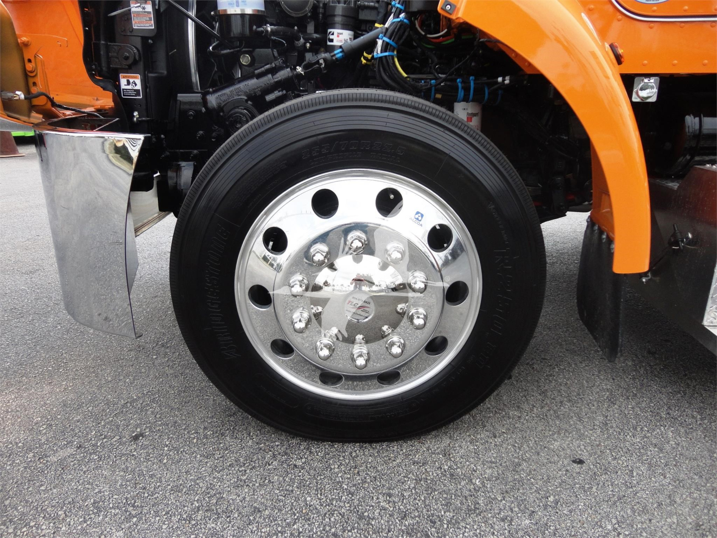 Peterbilt 337 front wheel and tire assembly showing polished steel hub with multiple lug nuts and orange fender in view.