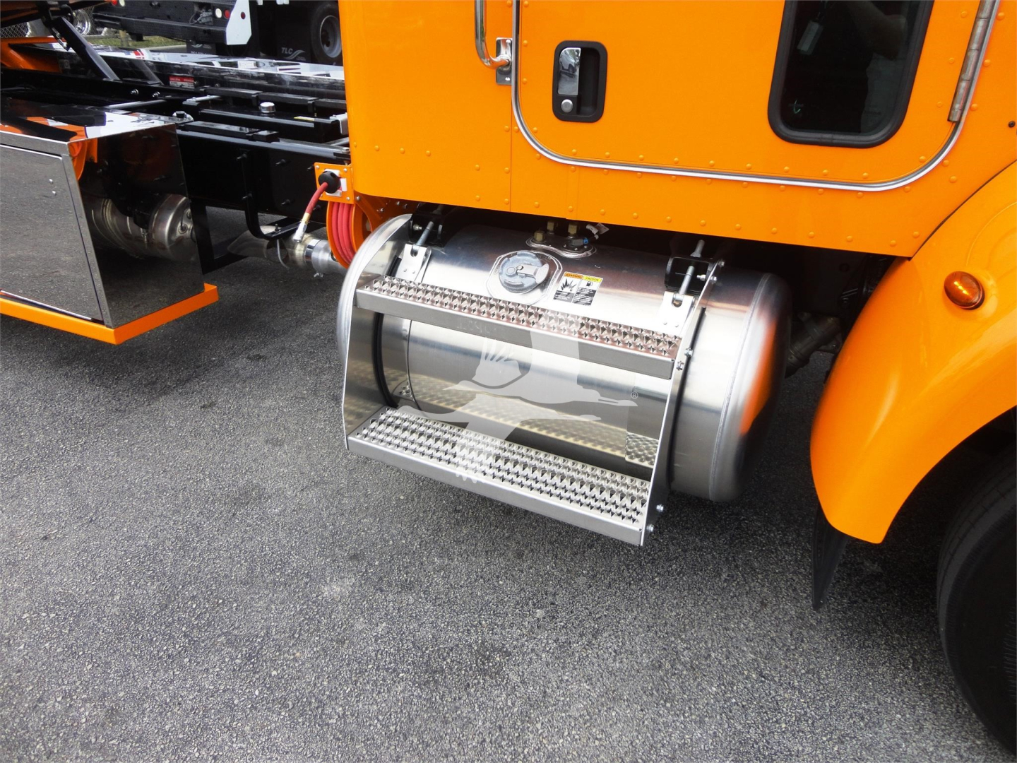 Truck side showing stainless steel fuel tank and chrome steps under an orange Peterbilt cab.
