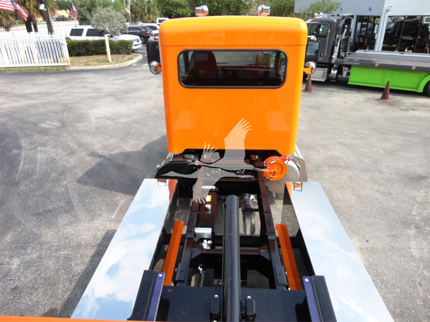 Orange Peterbilt 337 cab forward truck viewed from rear with rollback chassis and black drive shaft; chrome side rails and bright orange cab.
