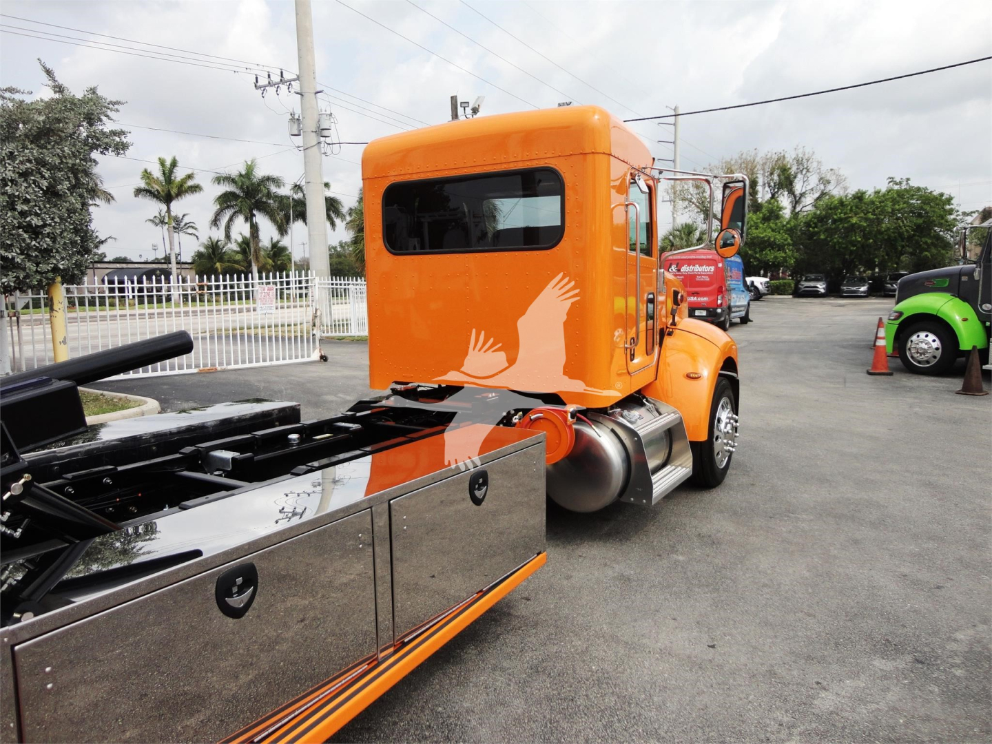 Orange Peterbilt 337 truck cab and rollback chassis with chrome toolboxes on the side, rear view showing cab window and wheel area.