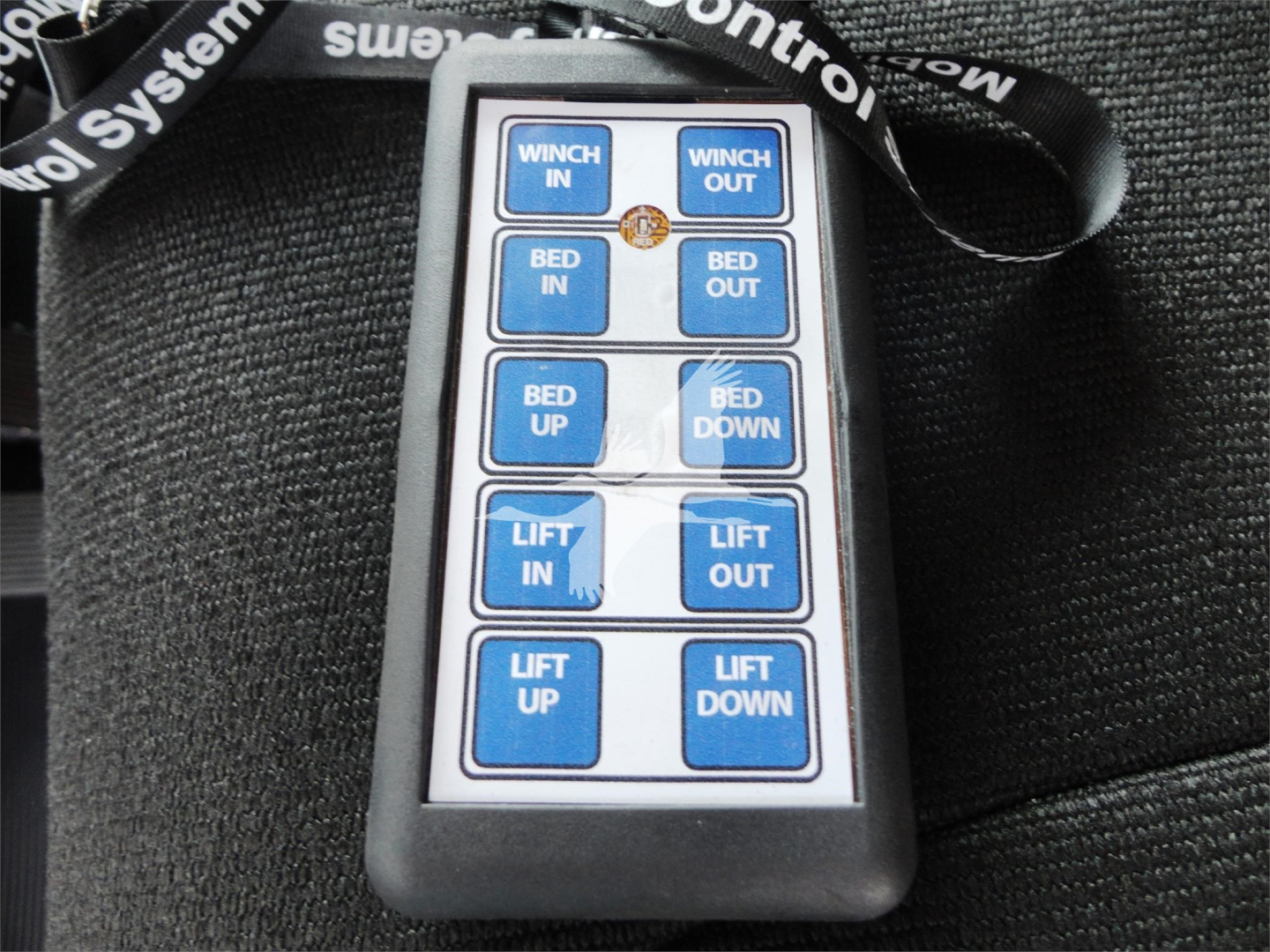Remote control panel showing blue buttons labeled WINCH IN, WINCH OUT, BED IN, BED OUT, BED UP, BED DOWN, LIFT IN, LIFT OUT, LIFT UP, LIFT DOWN on a black case.