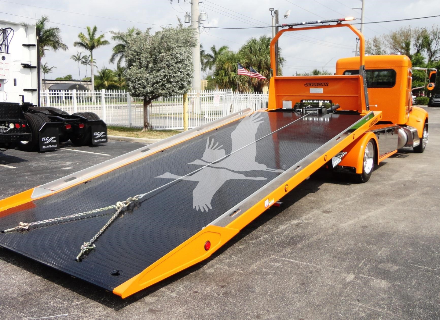 Peterbilt 337 rollback with bright orange cab and black loading ramp showing a white bird graphic.