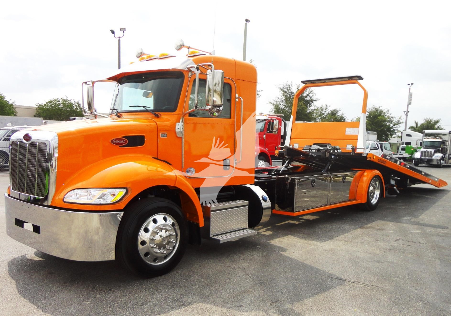 Orange Peterbilt 337 rollback tow truck shown in profile with flatbed and rear loading ramp.