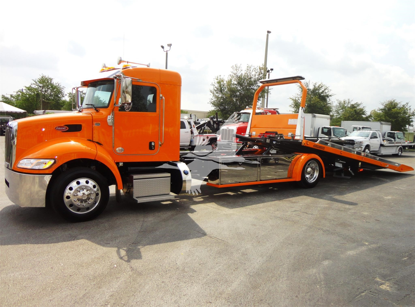 Peterbilt 337 rollback tow truck in orange, side view with flatbed ramp extended.