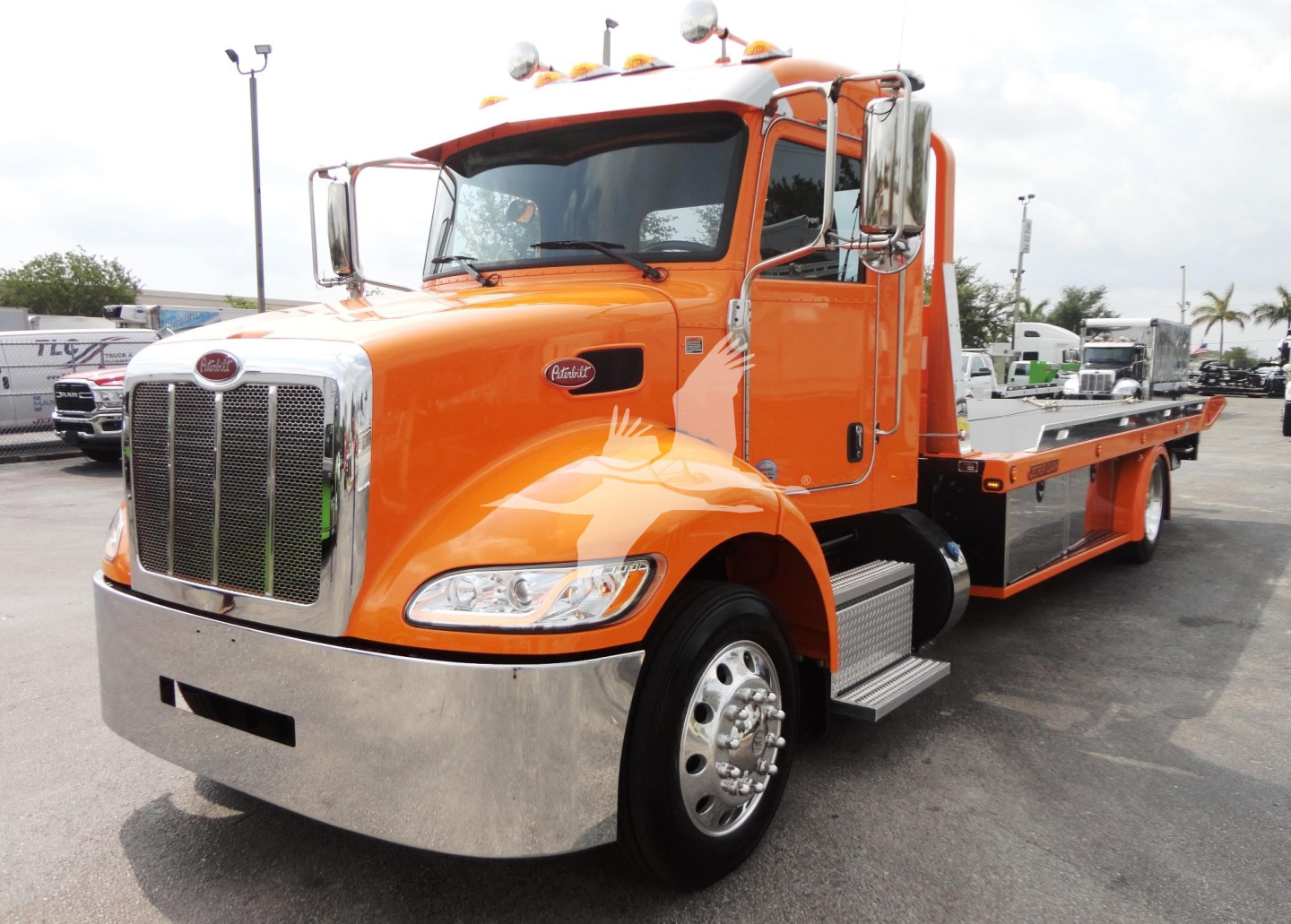 Peterbilt 337 rollback tow truck in orange with chrome front bumper and flatbed, side steps, grille, dual mirrors, and logo visible.