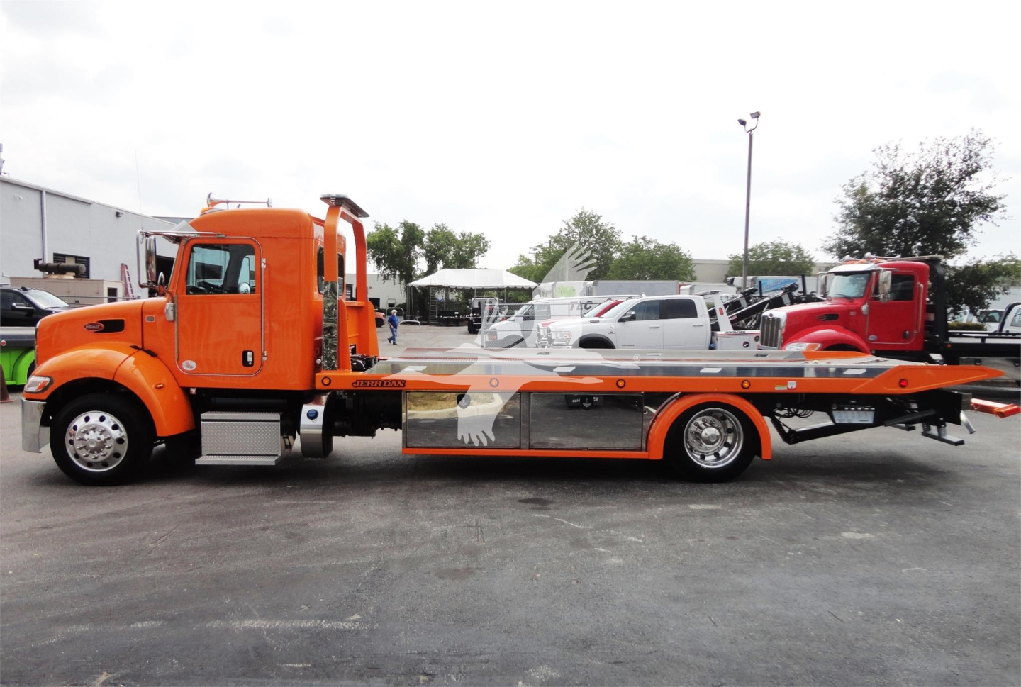 Peterbilt 337 rollback tow truck side view showing bright orange cab and flatbed with graphic and equipment.