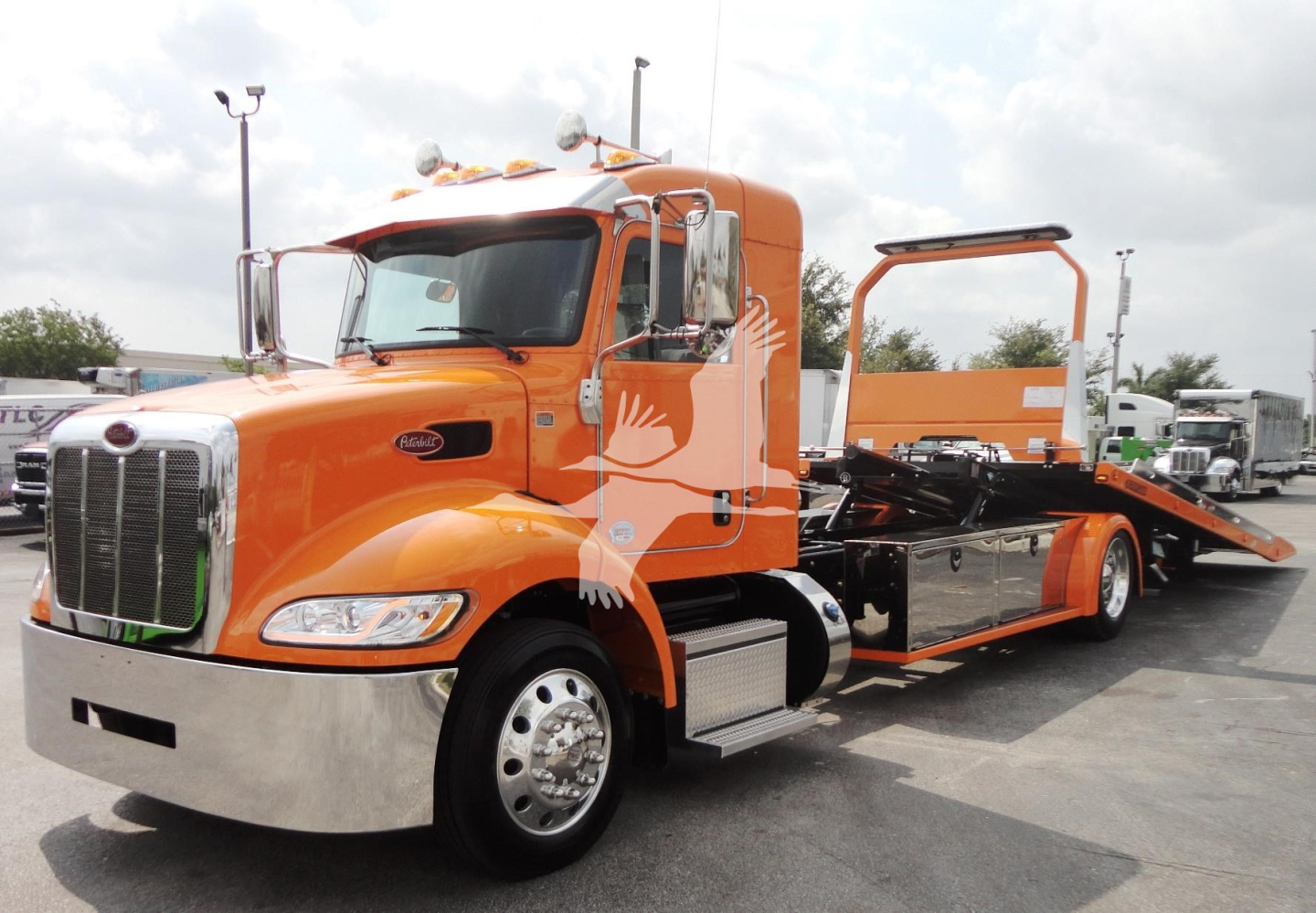 Peterbilt 337 rollback truck in orange with flatbed and wheel lift seen from front-left angle showing chrome bumper and side mirrors.