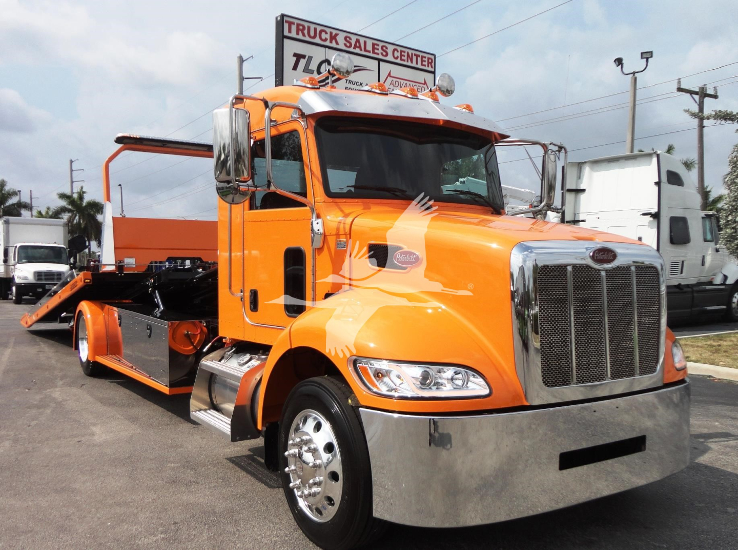 Peterbilt 337 rollback tow truck in orange with chrome bumper and flatbed, front grille, dealership in background
