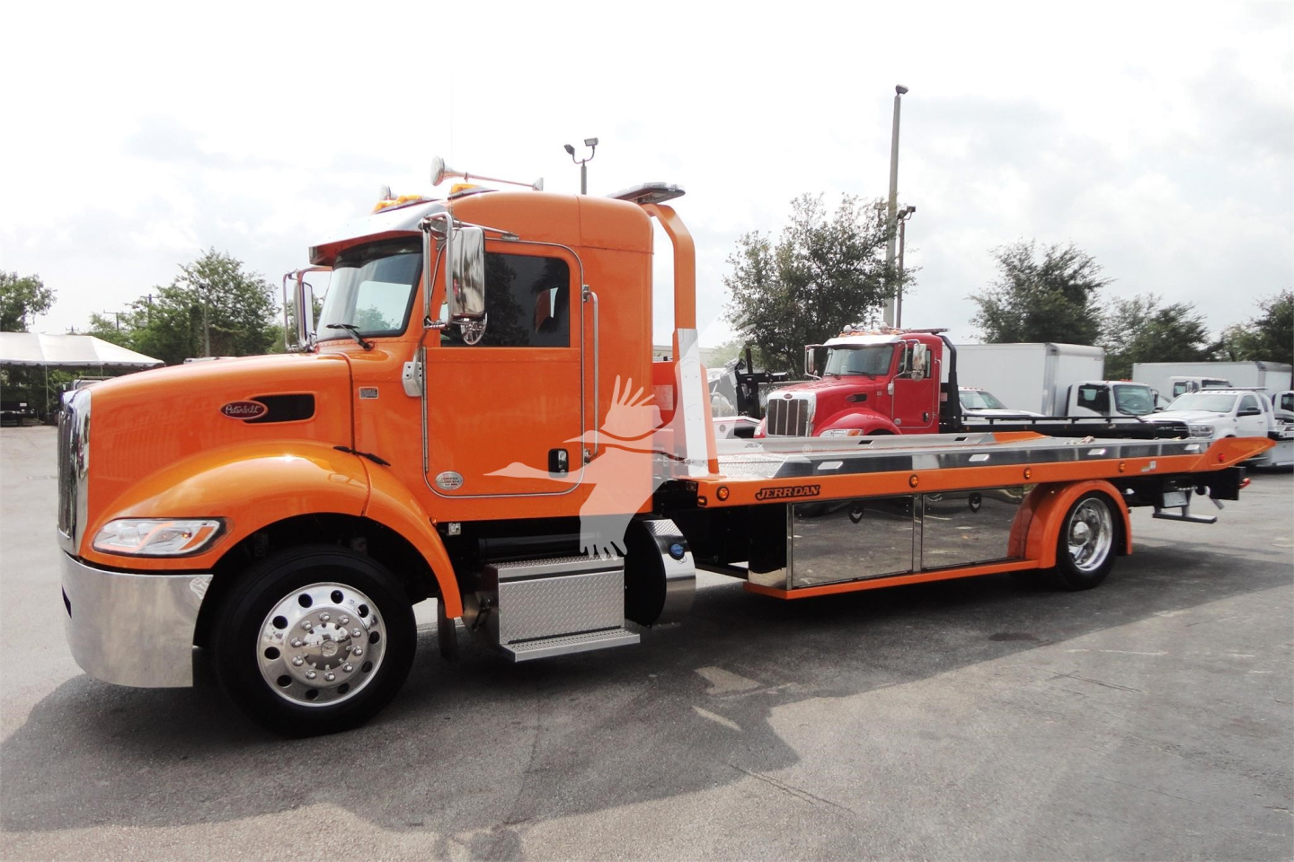 Orange Peterbilt 337 rollback truck viewed at side with flatbed tow setup and chrome wheels, stock number J06176, new unit.
