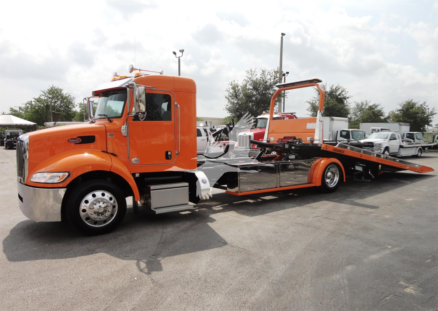 Peterbilt 337 rollback truck in orange with flatbed and loading ramp, side view.