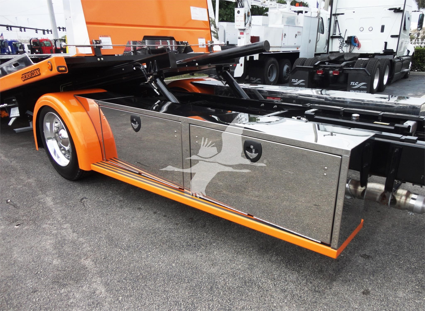 Peterbilt 337 rollback truck side view showing chrome tool/storage compartments and orange body with hydraulic lift arm.