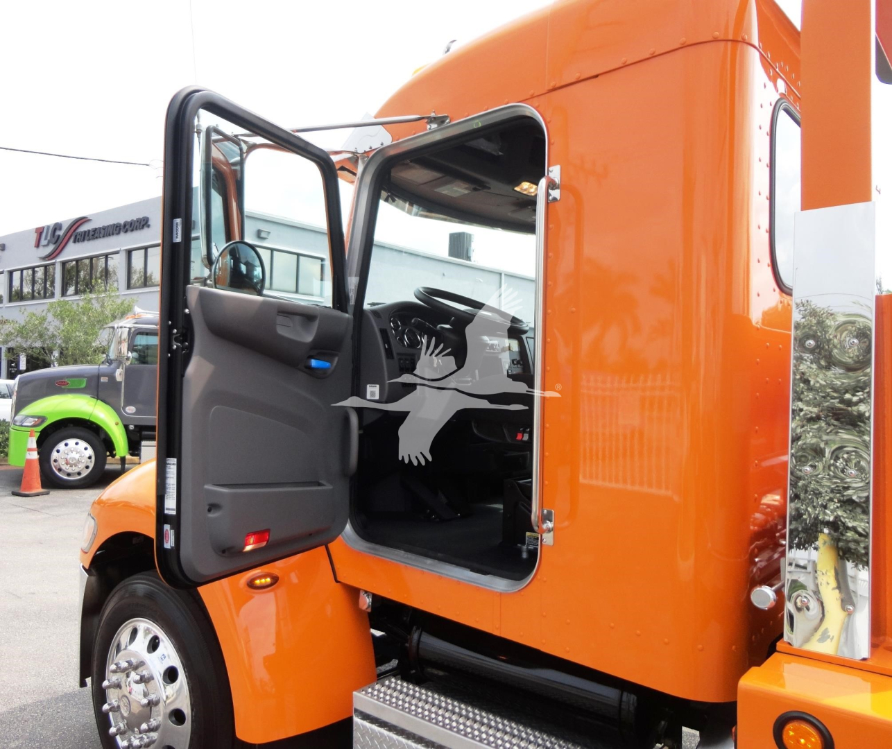 Peterbilt 337 truck cab with open door, orange exterior, showroom or dealership lot in background.