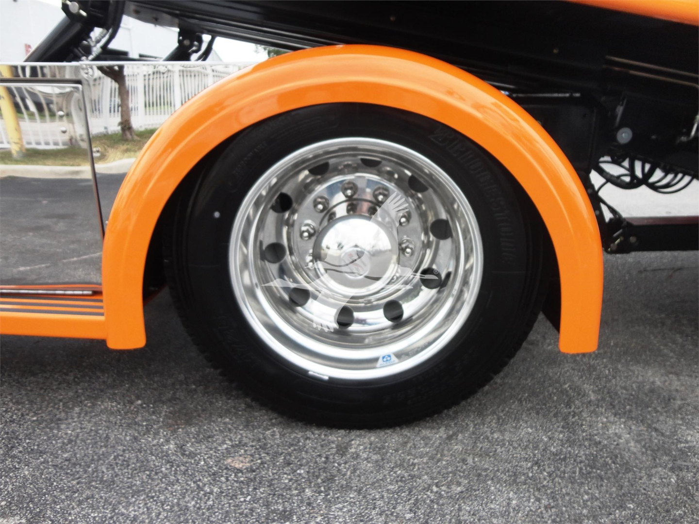 Wheel well and chrome front wheel of a Peterbilt 337 truck with orange fender flare, close-up view showing polished hubcap and tire.