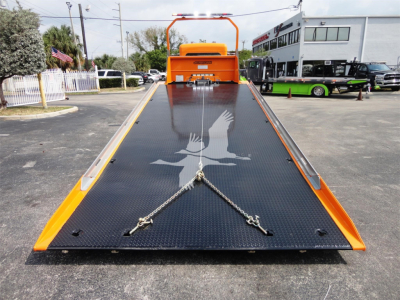 Front-facing view of a bright orange 2022 Peterbilt 337 rollback bed with a black diamond-plate steel ramp, eagle decal, and towing chains centered on the ramp.