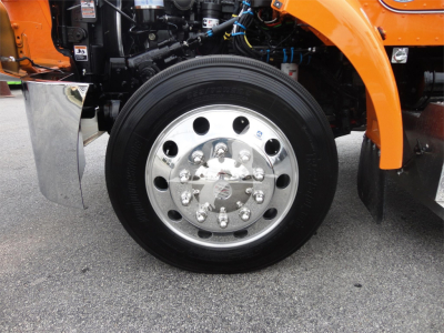 Peterbilt 337 front wheel and tire assembly showing polished steel hub with multiple lug nuts and orange fender in view.