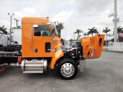 Orange Peterbilt 337 cab with hood open showing engine bay and chrome front wheel, rollback truck in lot.