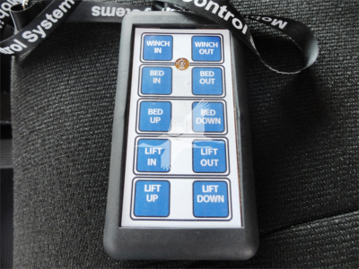 Remote control panel showing blue buttons labeled WINCH IN, WINCH OUT, BED IN, BED OUT, BED UP, BED DOWN, LIFT IN, LIFT OUT, LIFT UP, LIFT DOWN on a black case.