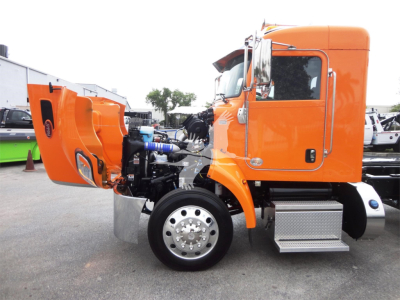 Peterbilt 337 rollback truck side view with hood open showing engine area and front wheel, bright orange cab and chrome steps.