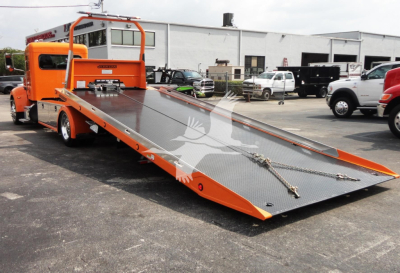 Peterbilt 337 rollback tow truck with orange finish and a tilted flatbed ramp in an open lot.