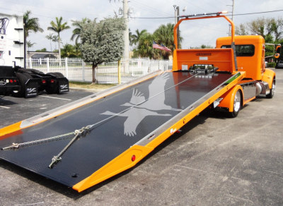 Peterbilt 337 rollback with bright orange cab and black loading ramp showing a white bird graphic.