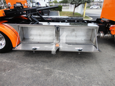 Two open aluminum storage boxes mounted under a Peterbilt 337 rollback truck, showing interior compartments and latch handles.