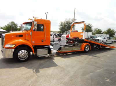 Peterbilt 337 rollback tow truck in orange, side view with flatbed ramp extended.