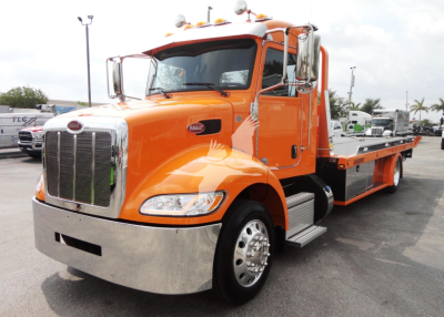 Peterbilt 337 rollback tow truck in orange with chrome front bumper and flatbed, side steps, grille, dual mirrors, and logo visible.