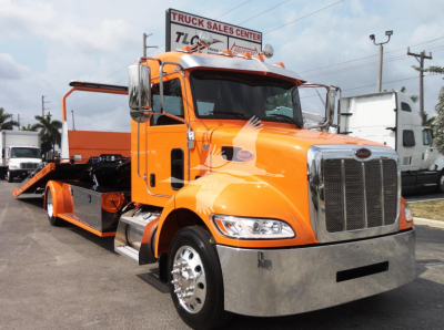 Peterbilt 337 rollback tow truck in orange with chrome bumper and flatbed, front grille, dealership in background