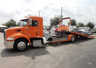 Peterbilt 337 rollback truck in orange with flatbed and loading ramp, side view.