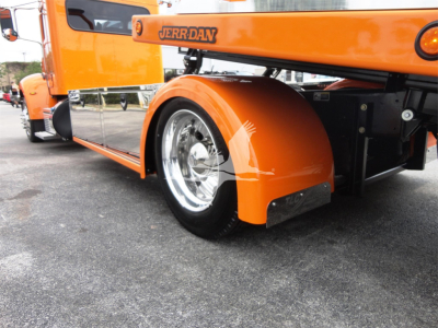 Peterbilt 337 rollback truck rear wheel and fender view showing orange paint, chrome wheel, and Jerr-Dan equipment arm.