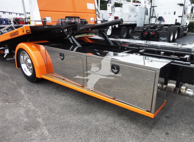 Peterbilt 337 rollback truck side view showing chrome tool/storage compartments and orange body with hydraulic lift arm.